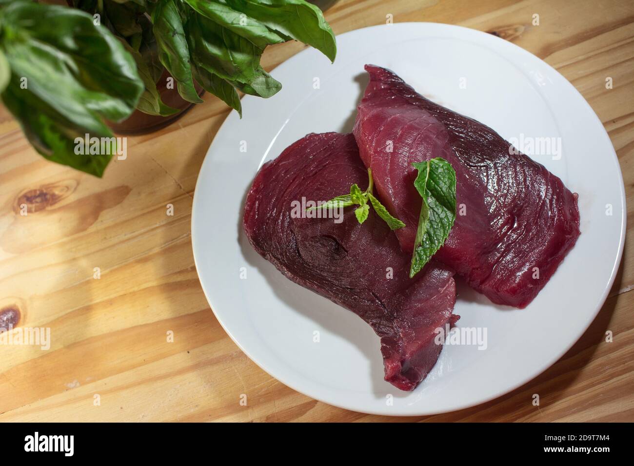 Two slices of raw fresh bluefin tuna on a plate with mint and basil Stock Photo