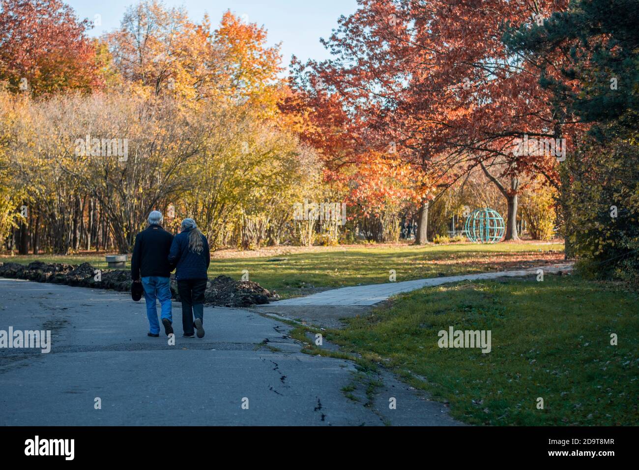 An elderly couple taking a walk in a park. Orange autumn colours around ...