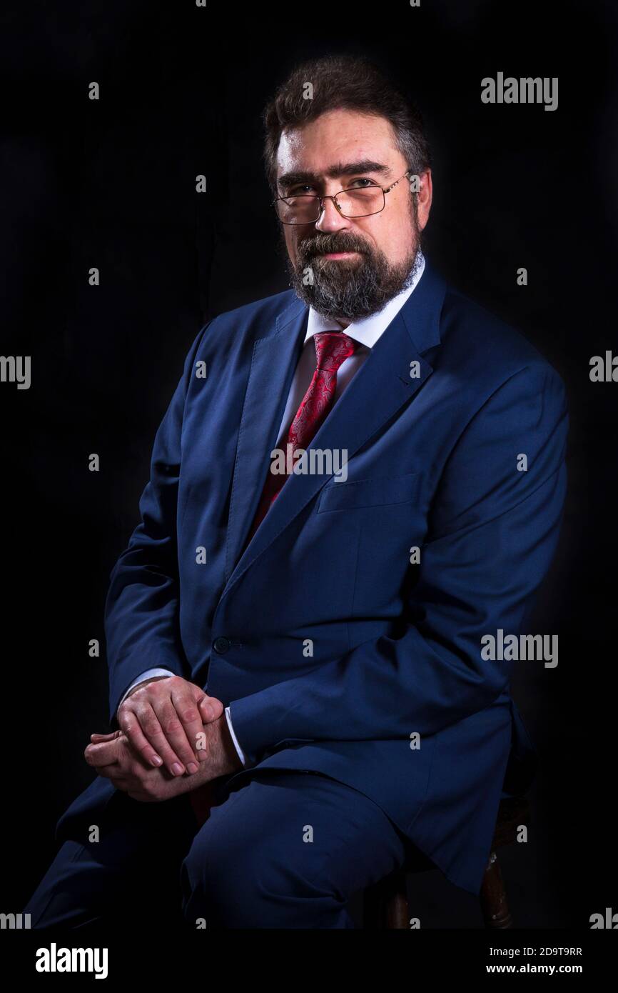 Mature businessman dressed in blue suit with red tie studio portrait ...