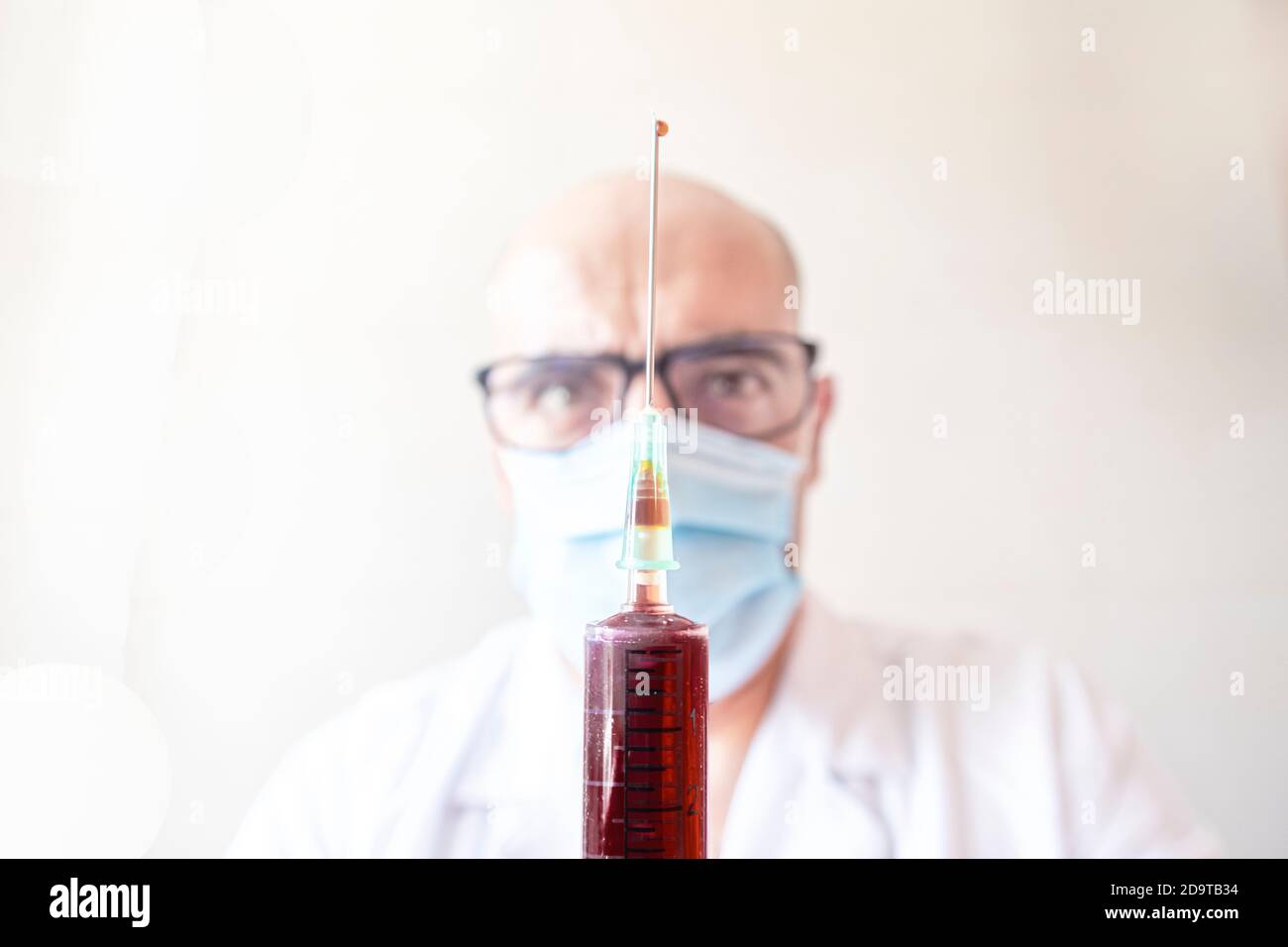 closeup of a blood syringe with a drop on the tip of the needle with the doctor out of focus in the background selective focus Stock Photo