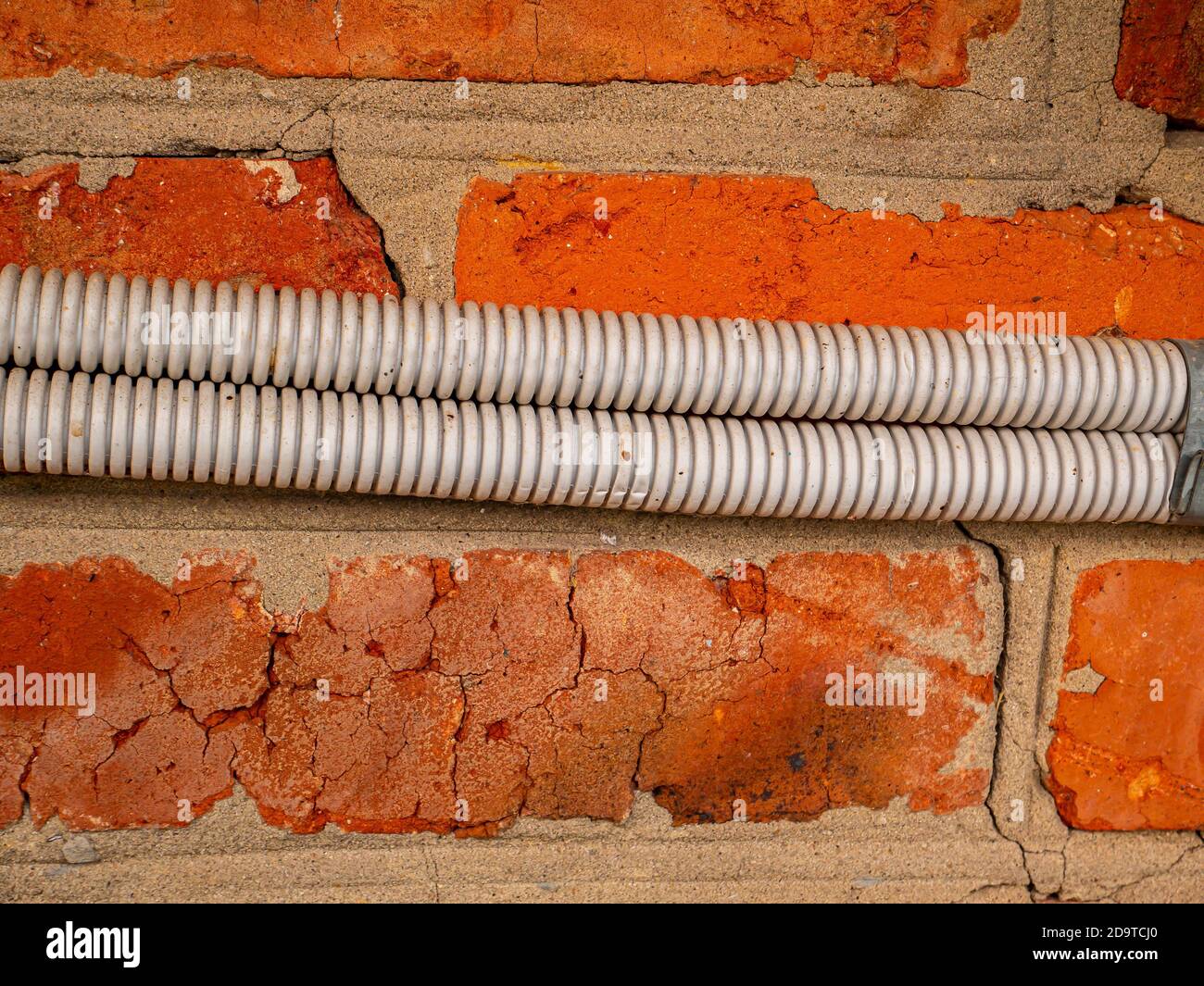 Electrical wiring in plastic corrugation on a brick wall Stock Photo