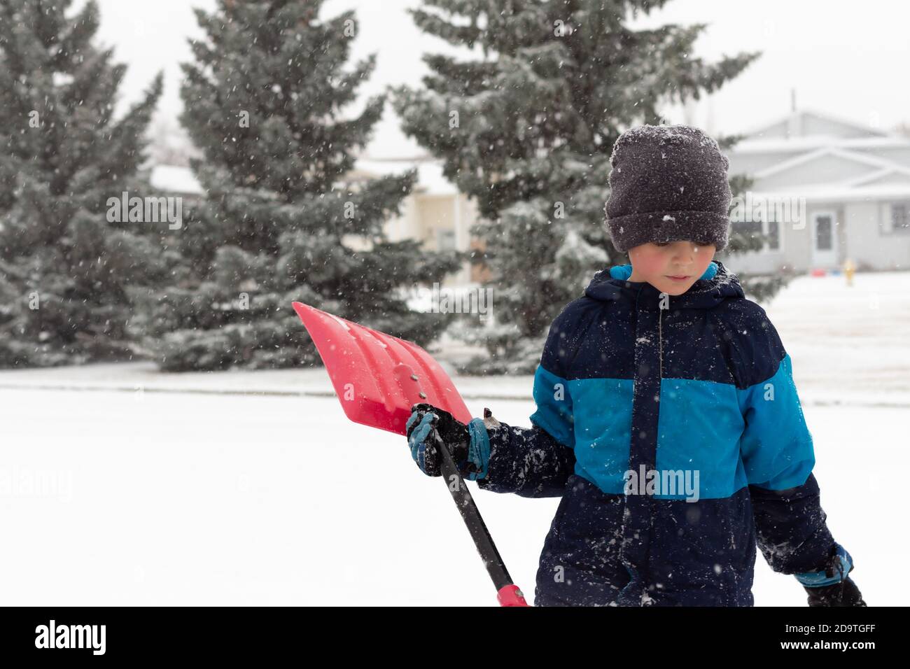 child with snow shovel looking down while standing outside during snow storm Stock Photo