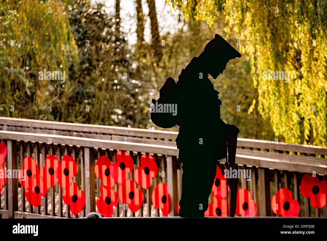 A cast iron silhouette of a soldier with head bowed and a footbridge covered in poppies over the River Mole in Brockham, Surrey for remembrance day Stock Photo