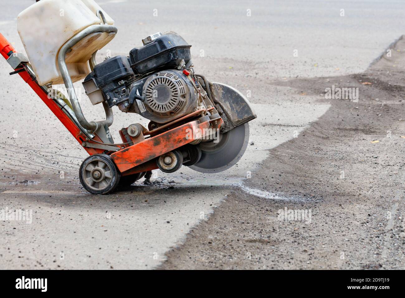 Petrol cutter with working diamond cut-off wheel ready to go against the background of old asphalt in blur, copy space. Stock Photo