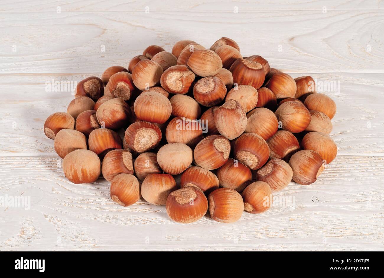Pile of unpeeled hazelnuts over white wood table. Nuts as an antioxidant and protein source for ketogenic diet and vegetarianism. Top view. Stock Photo