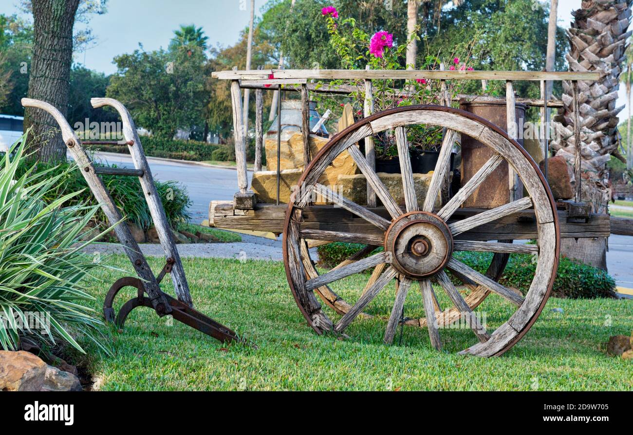 Vintage weathered wagon cart and old plow displayed as lawn decorations in a suburban area. Stock Photo