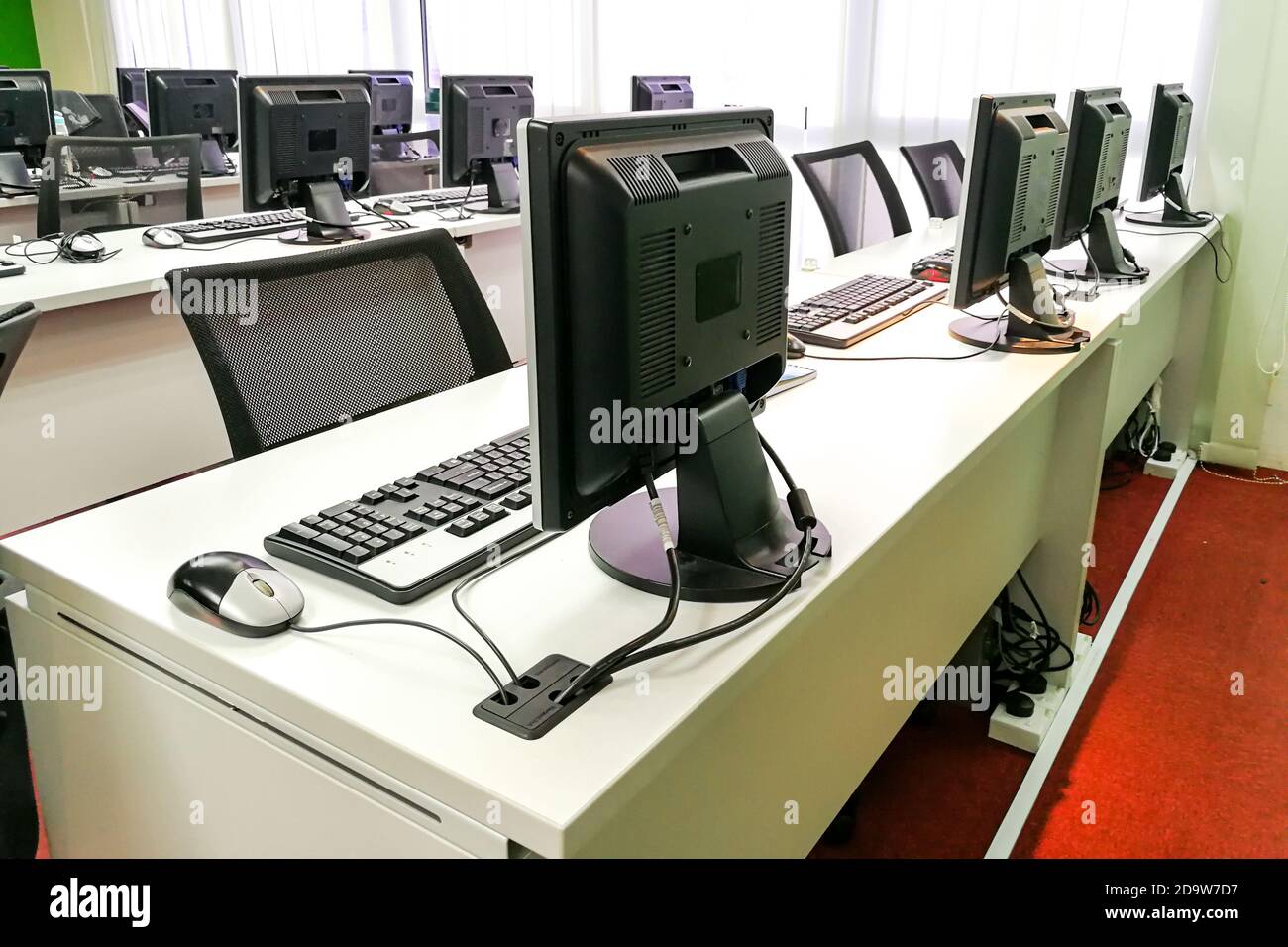 Empty computer classroom with monitors on top of table Stock Photo