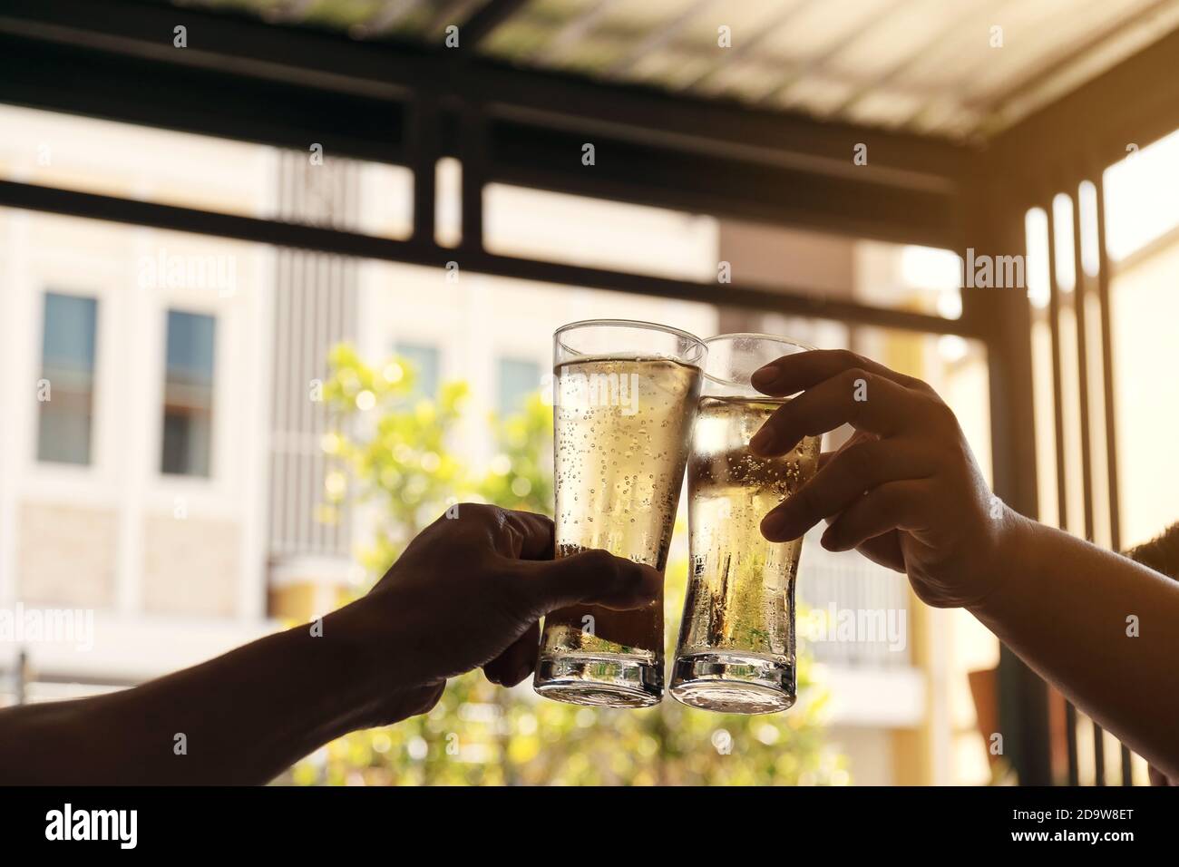 The hands of two men holding a glass of beer raised together to drink to celebrate the success. Stock Photo