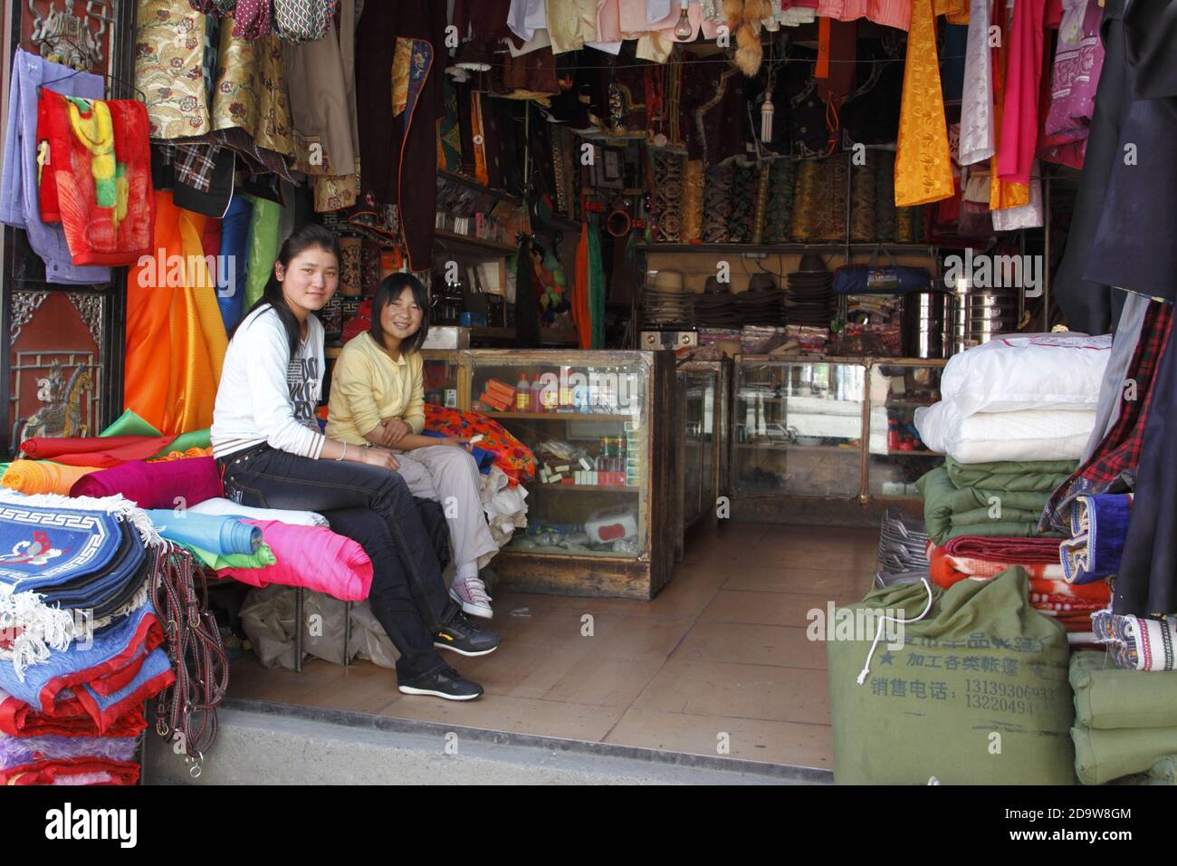 Two young Chinese women attending a store selling carpets, clothing and other Yak Herder essentials, Xingduqiao, west Sichuan Province June 2011 Stock Photo