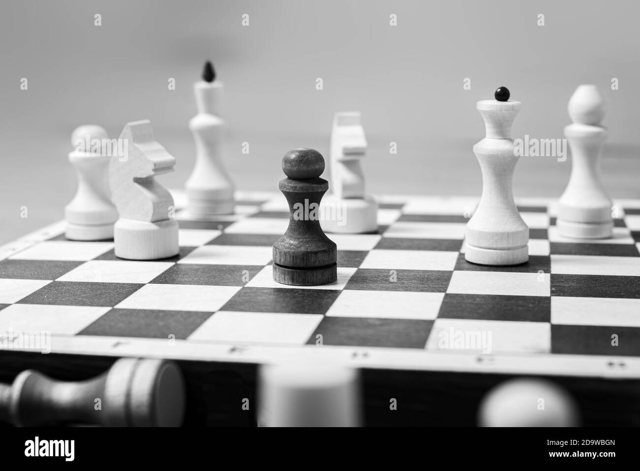One black pawn stands against a whole board of white chess pieces, selective focus, copy space. The concept is one against all. Leadership concept among competitors Stock Photo
