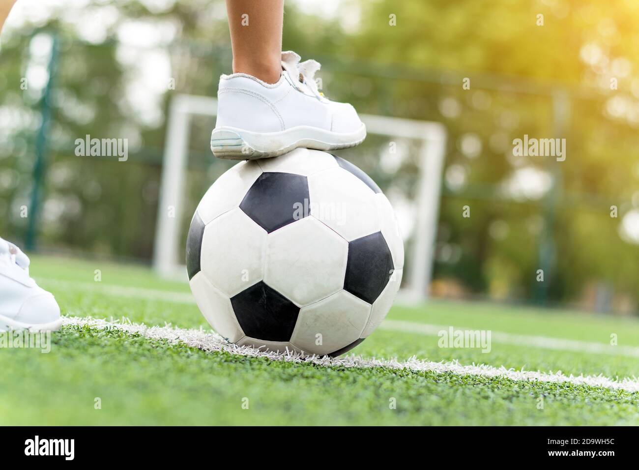 Feet of a boy wearing white sneakers stepping on a soccer ball in the middle of the football