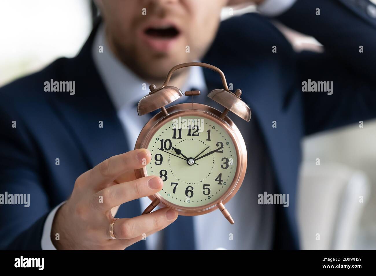 Worried young male manager employee in formal wear holding clock. Stock Photo