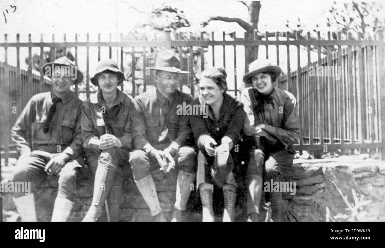 Group of men and women in uniform sitting in front of a fence   Stock Photo