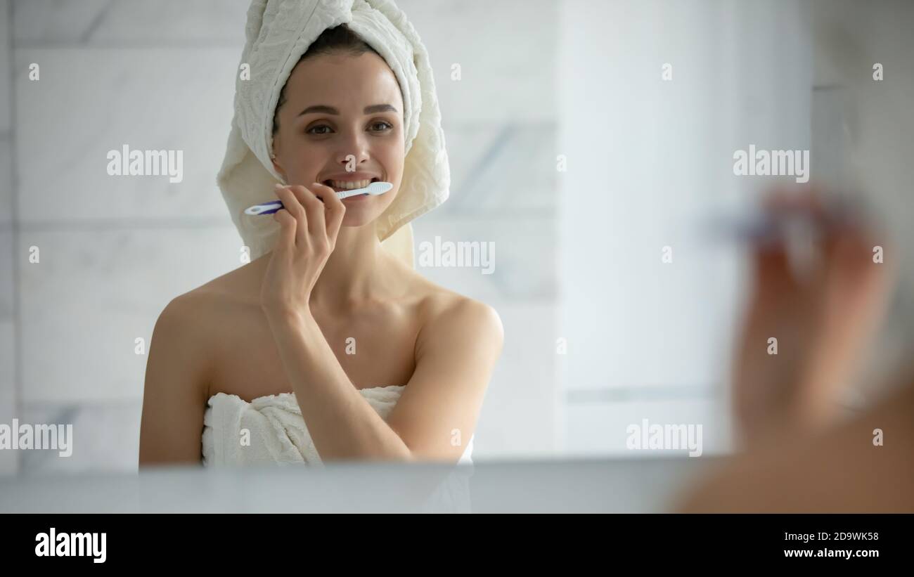 Attractive young lady wrapped in towel holding toothbrush cleaning