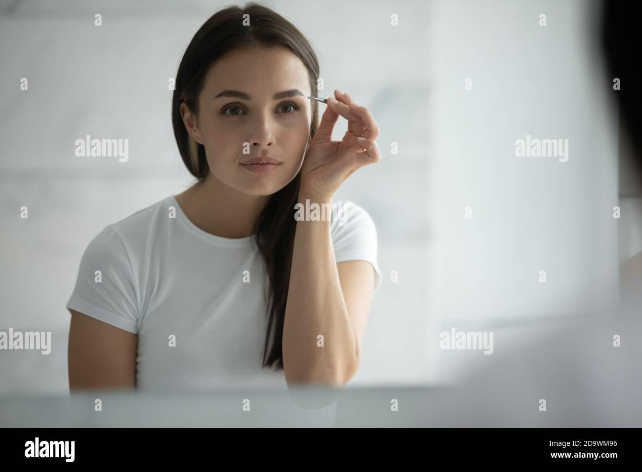 Concentrated young female doing sharp accurate eyebrow contours using tweezer Stock Photo