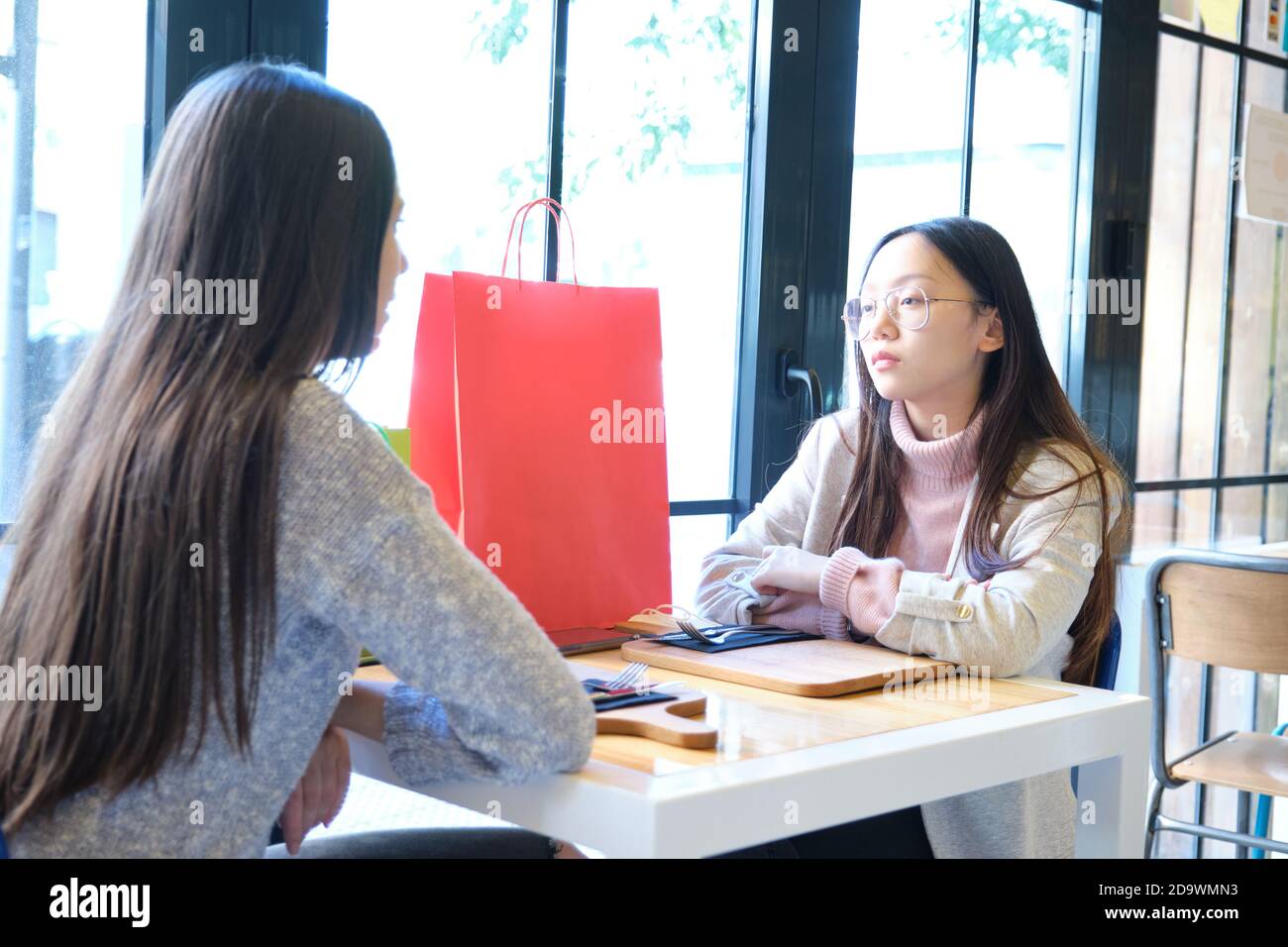 Two female friends in a coffee shop after shopping. Caucasian and asian women in a restaurant. Stock Photo