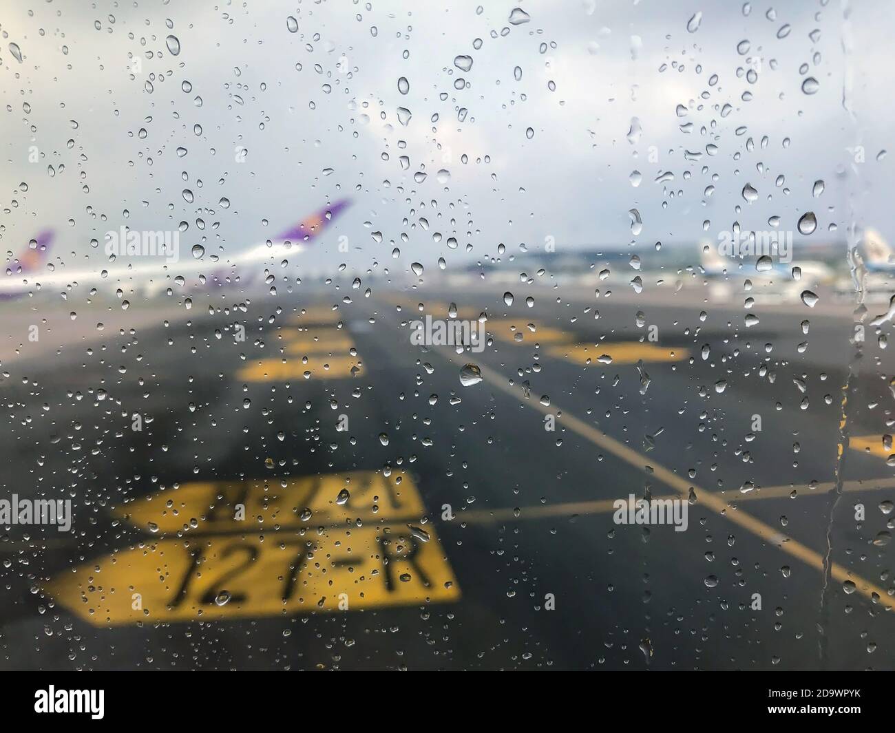 The rain drops on the glass outside of the passenger plane window that is parked on the runway. Stock Photo