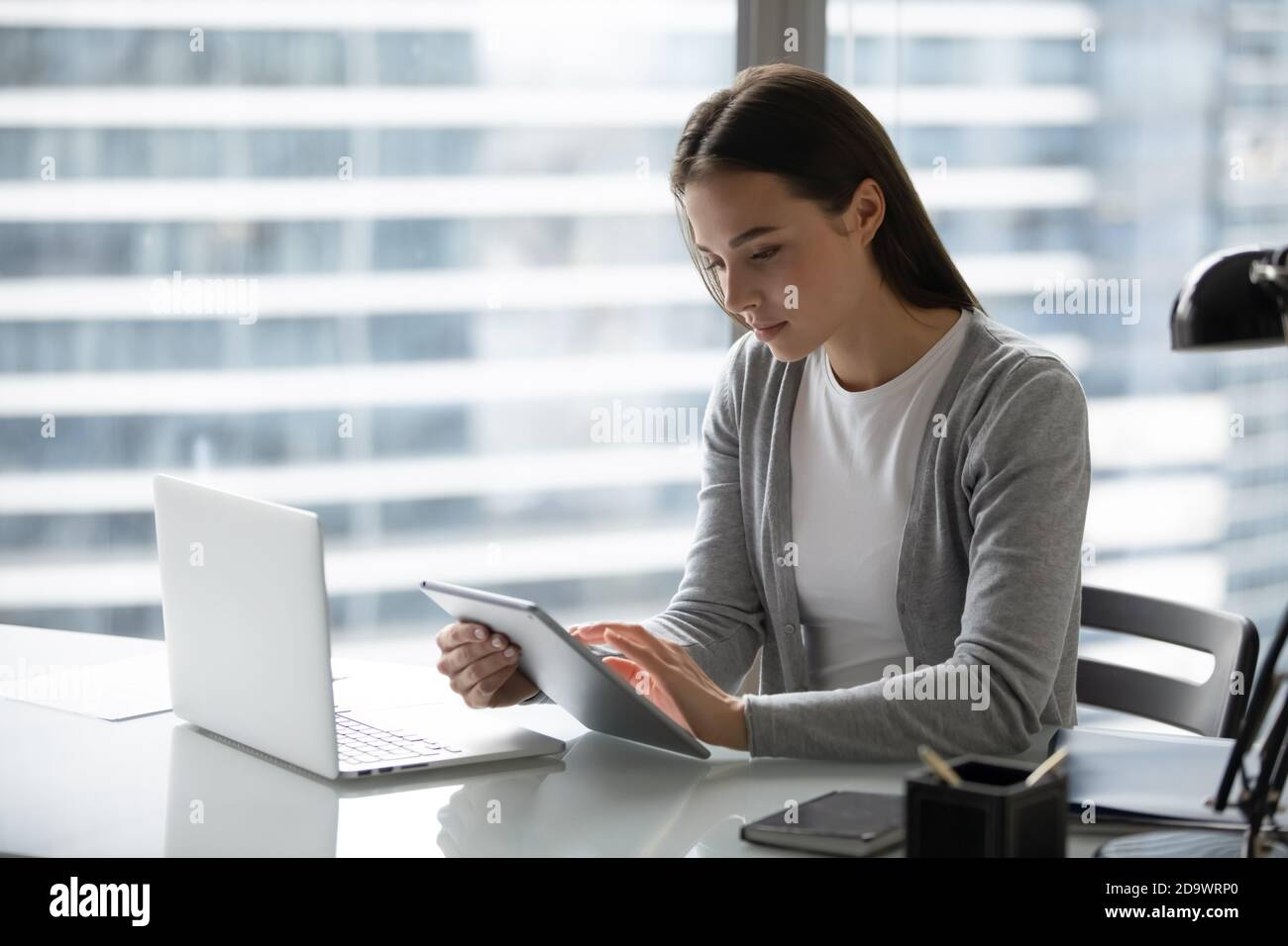 Concentrated young businesswoman synchronizing data at pad and laptop memory Stock Photo