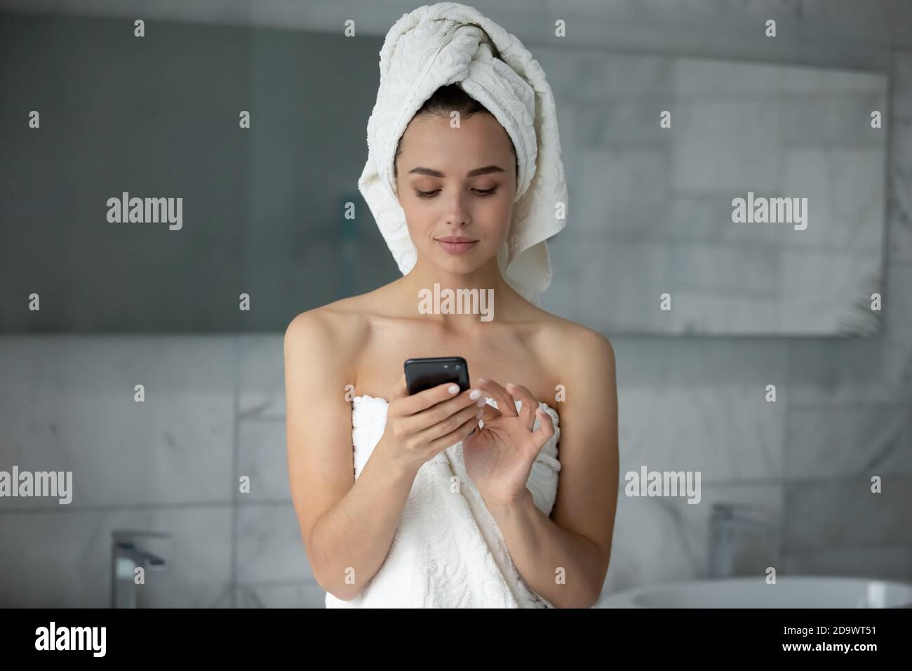 Confident positive young female using smartphone in bathroom texting message Stock Photo