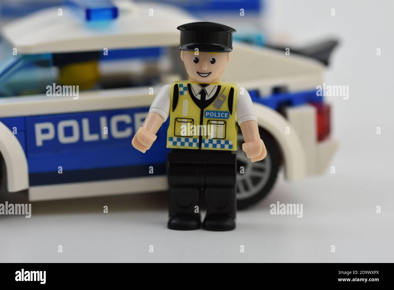 A Blox Policeman minifigure stood in Front of a toy Lego Police car Stock Photo