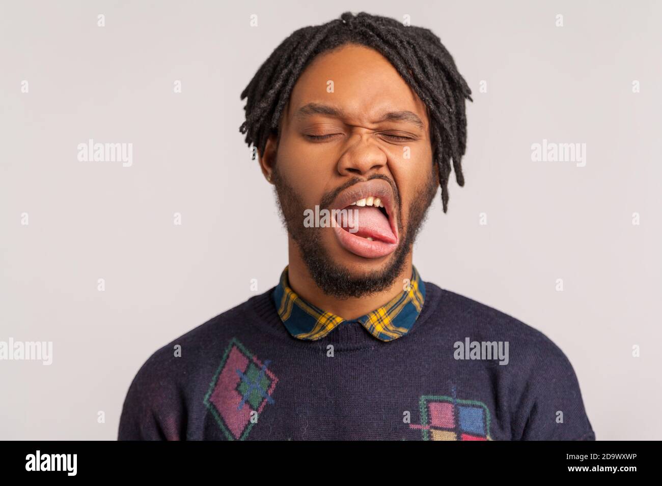 Closeup face of bearded african man with dreadlocks fooling face and grimacing feeling unpleasant taste or smell, disgust. Indoor studio shot isolated Stock Photo