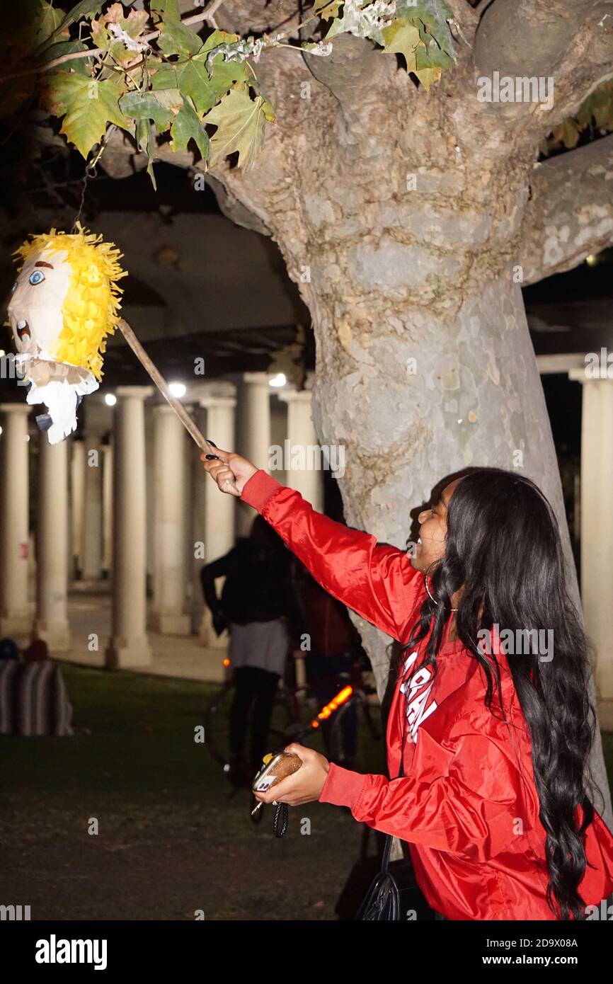 Oakland, California, USA. 7 Nov, 2020. Joe Biden/Kamala Harris supporters fill the streets to celebrate their victory over Donald Trump in the USA Presidential Election. A young woman hits the head of a Donald Trump piñata hanging from a tree with a stick in Vice President-elect Kamala Harris' hometown. Credit: Kristin Cato/Alamy Live News Stock Photo