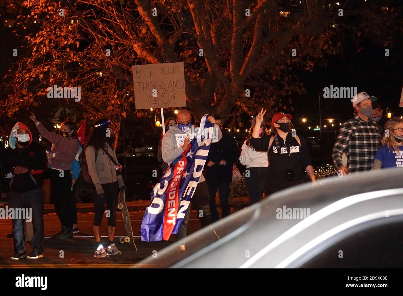 Oakland, California, USA. 7 Nov, 2020. Joe Biden/Kamala Harris supporters fill the streets to celebrate their victory over Donald Trump in the USA Presidential Election. Here they wave at a honking car caravan passing by Lake Merritt in Vice President-elect Kamala Harris' hometown. Credit: Kristin Cato/Alamy Live News Stock Photo