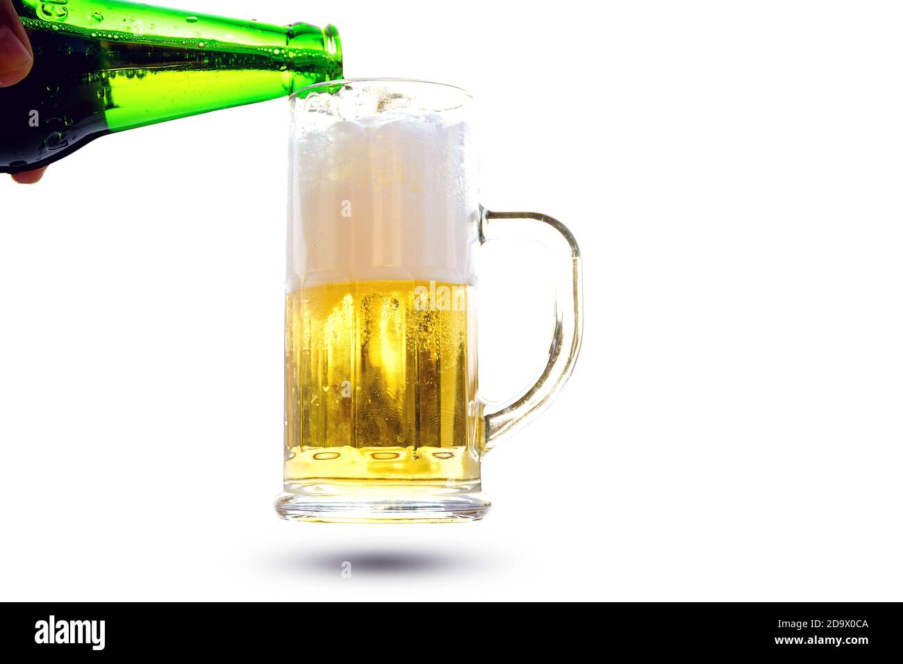 Pour beer from a bottle into a glass with a handle isolated on white background. Stock Photo