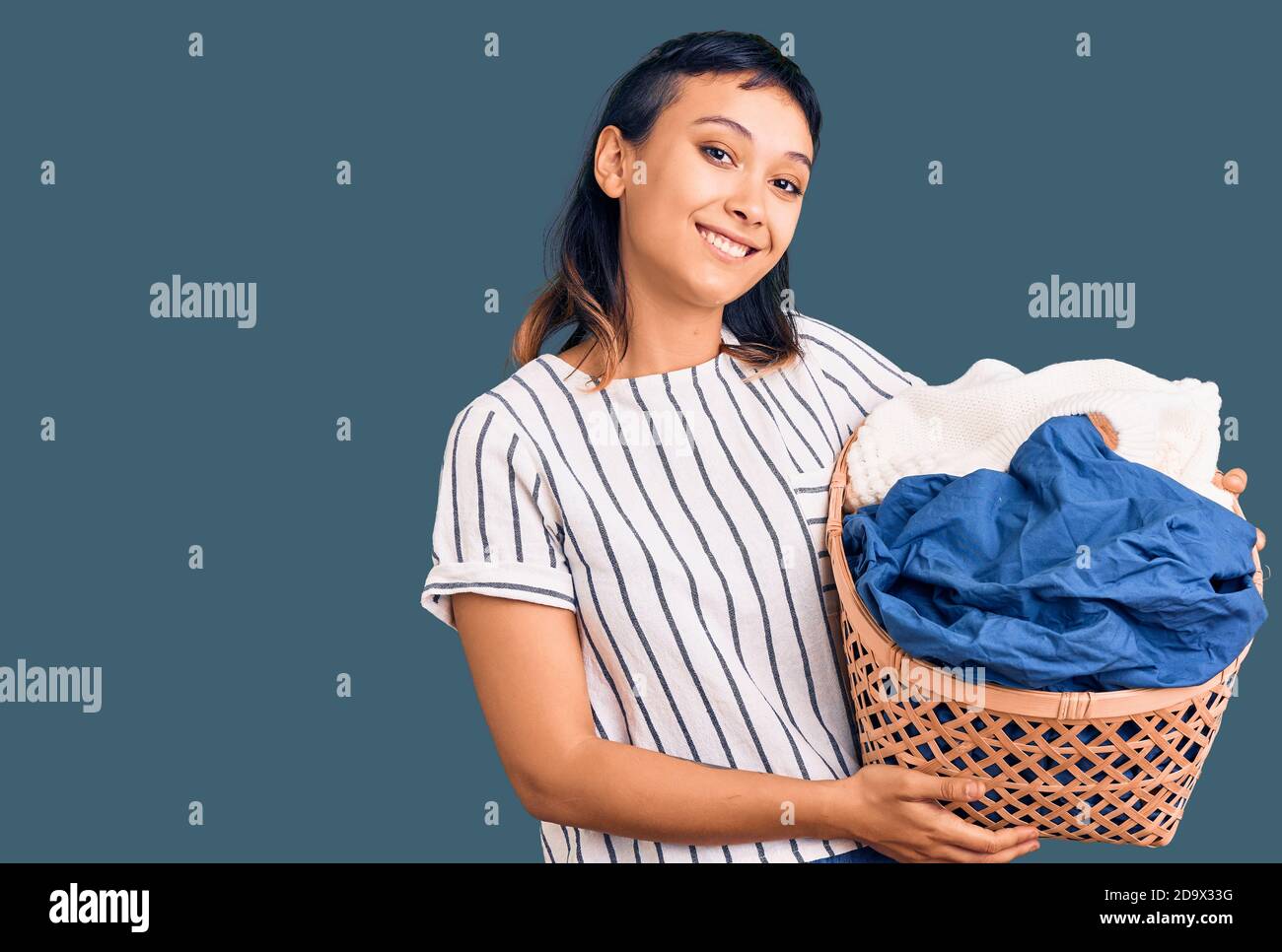 Young woman holding laundry basket looking positive and happy standing ...