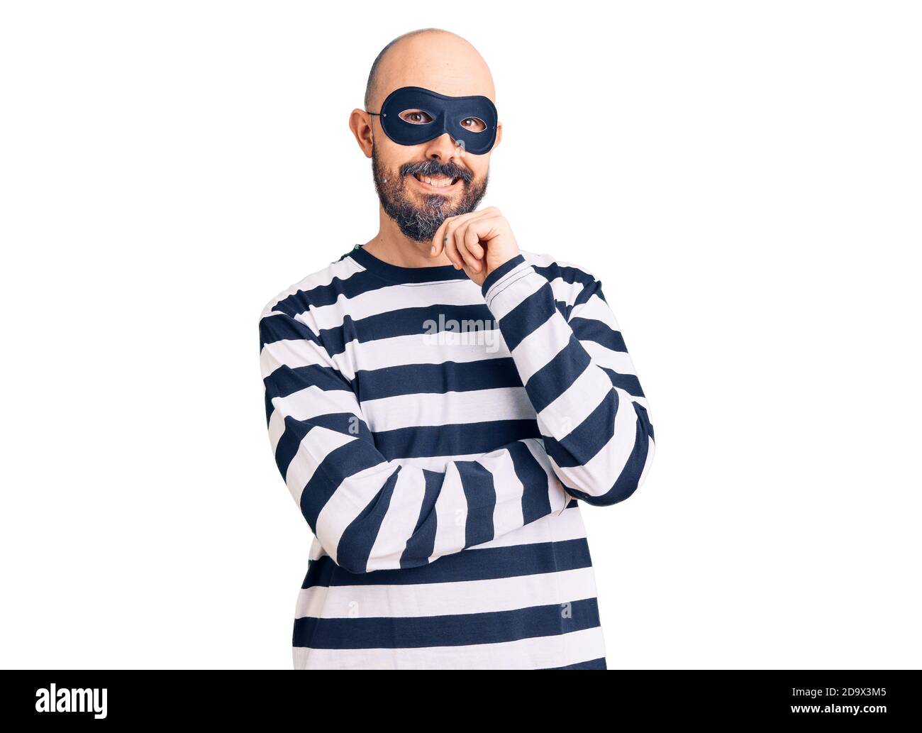 Young handsome man wearing burglar mask looking confident at the camera smiling with crossed arms and hand raised on chin. positive Stock Photo - Alamy