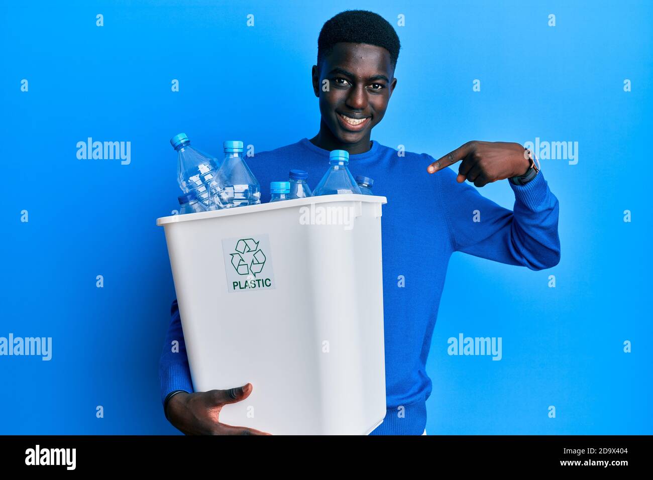 Young african american man holding recycling wastebasket with plastic bottles smiling happy pointing with hand and finger Stock Photo