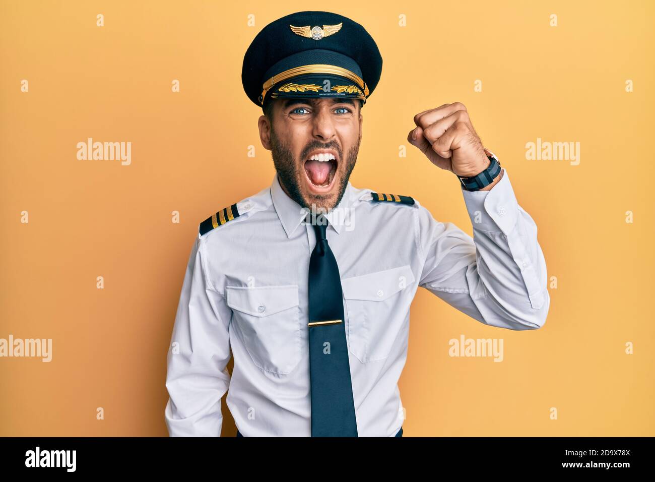 Handsome hispanic man wearing airplane pilot uniform angry and mad ...