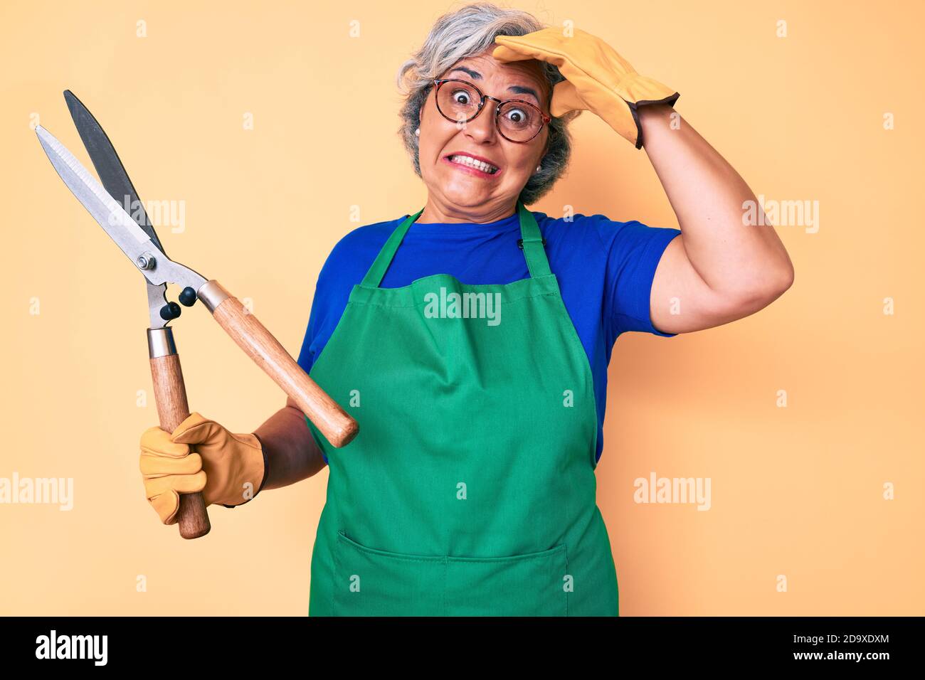 Senior hispanic woman wearing gardener apron and gloves holding shears ...