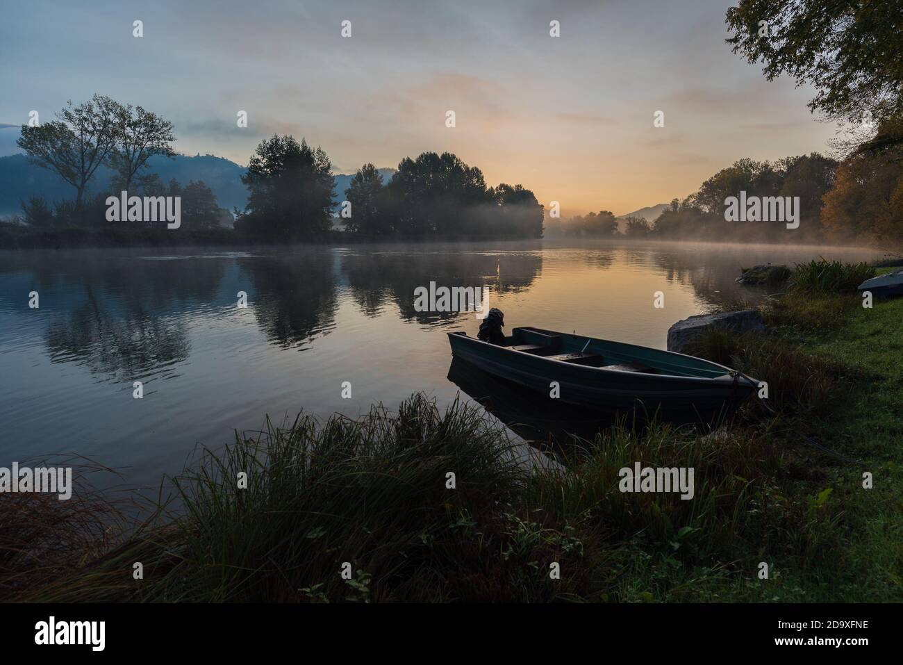 Calm scenic picture of small fishing boat on the Adda river on a hazy sunrise with foliage Stock Photo