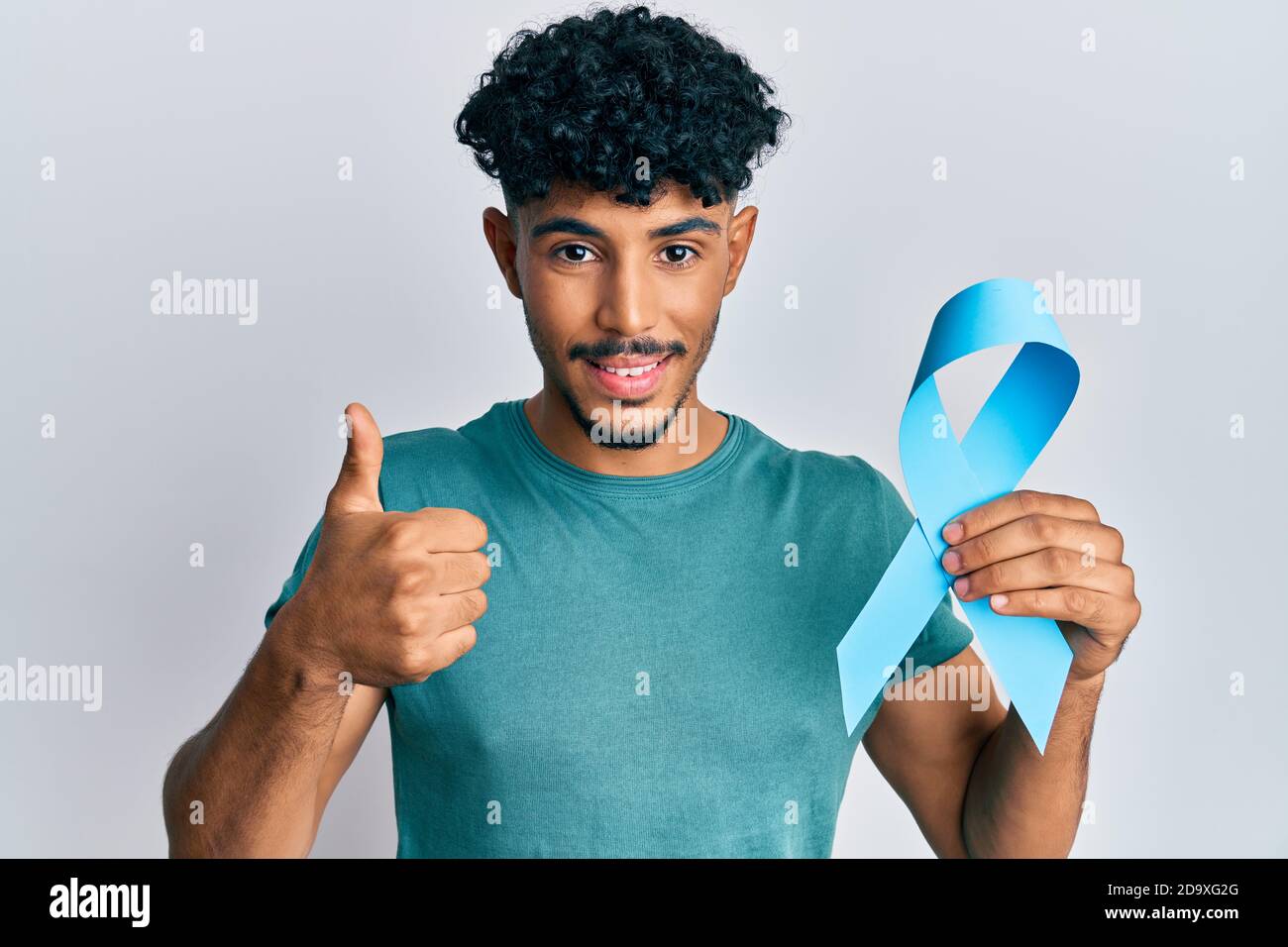 Young arab handsome man holding blue ribbon smiling happy and positive ...