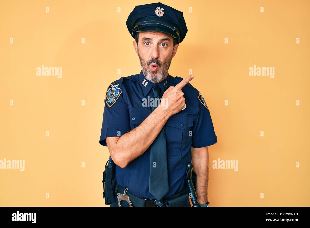 Middle age hispanic man wearing police uniform surprised pointing with ...