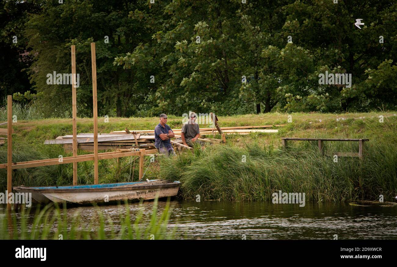 Men resting on the bank of the River Arun whilst building a wooden pontoon. Stock Photo