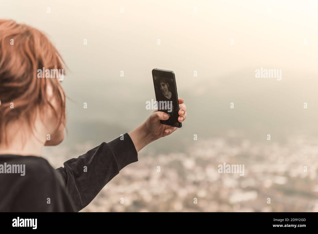 The red-haired girl taking photo with smart phone at the mountain peak ...