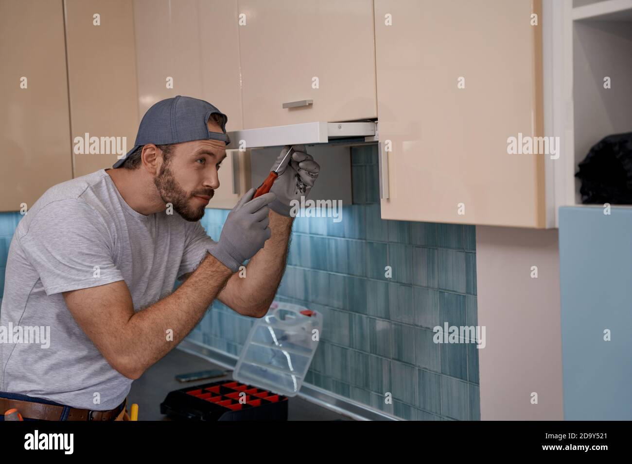 Young caucasian repairman installing kitchen hood using screwdriver Stock Photo