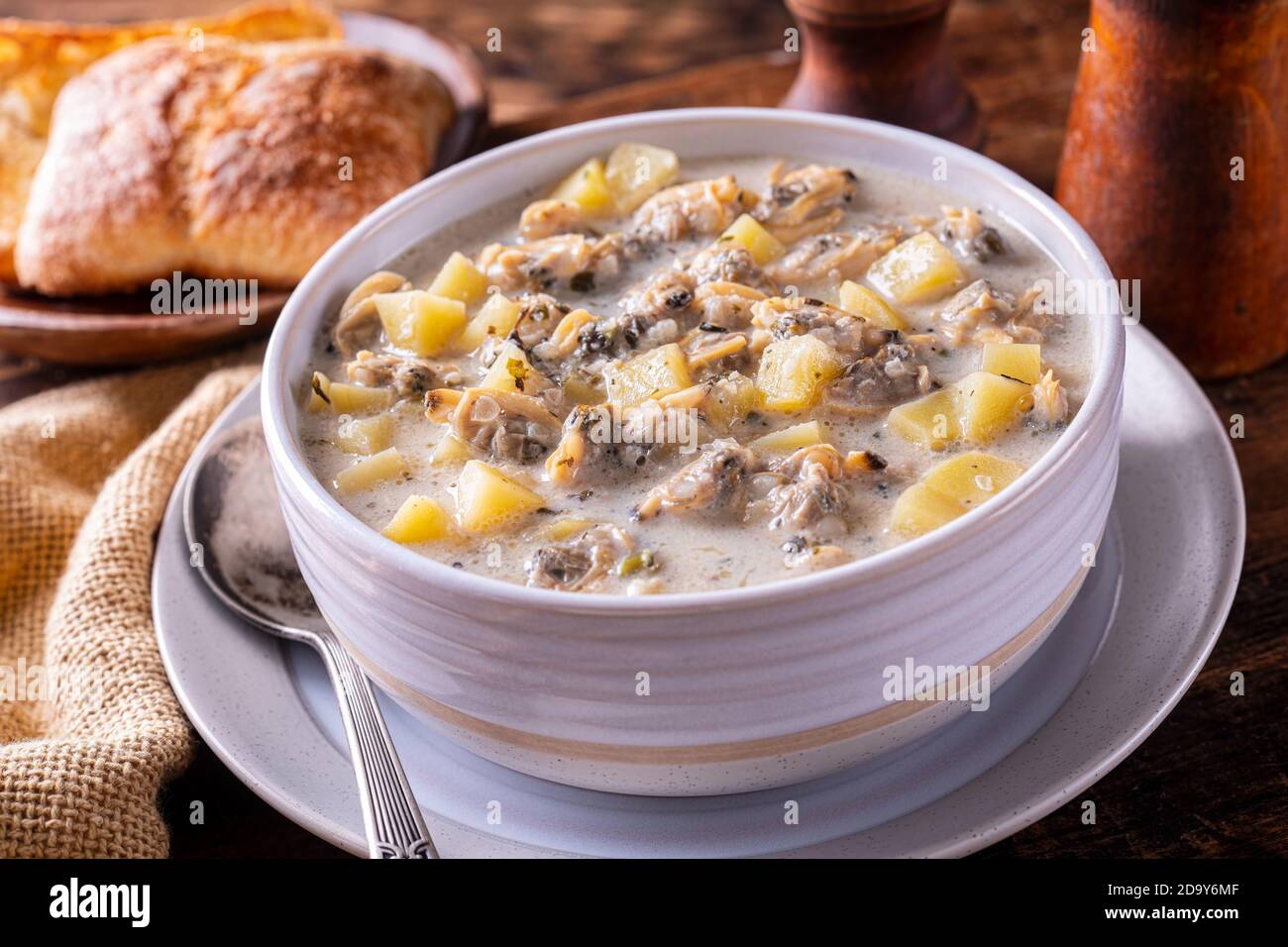 A bowl of creamy delicious clam chowder with potato, celery and onion on rustic wood table top. Stock Photo