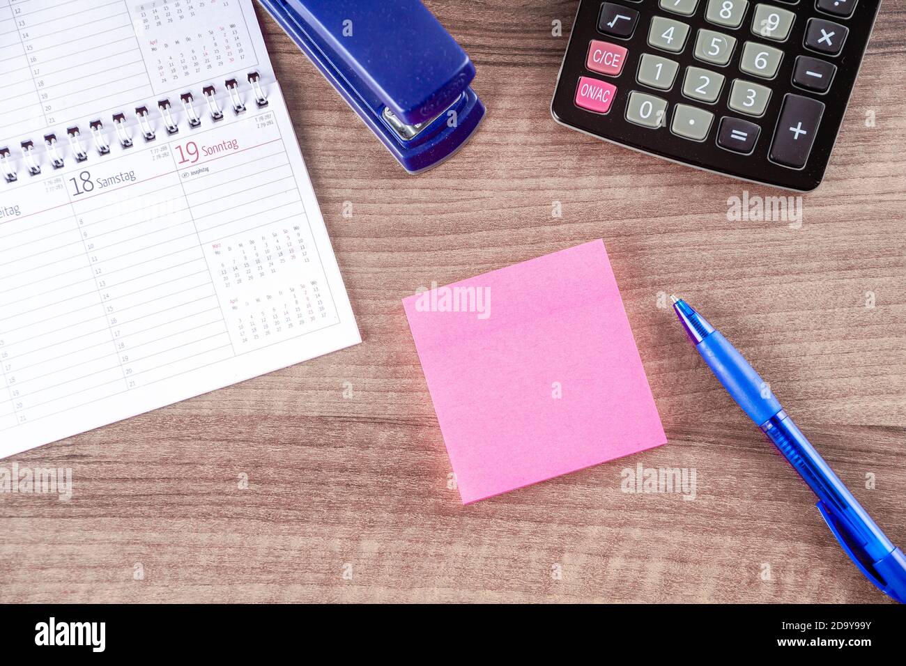Flat lay of a business desk with a calendar, a calculator and a pen