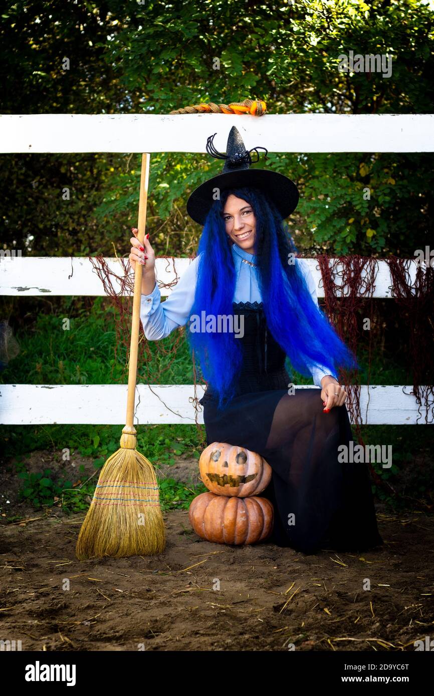 A girl in a witch costume sits on two pumpkins and holds a broom in her ...