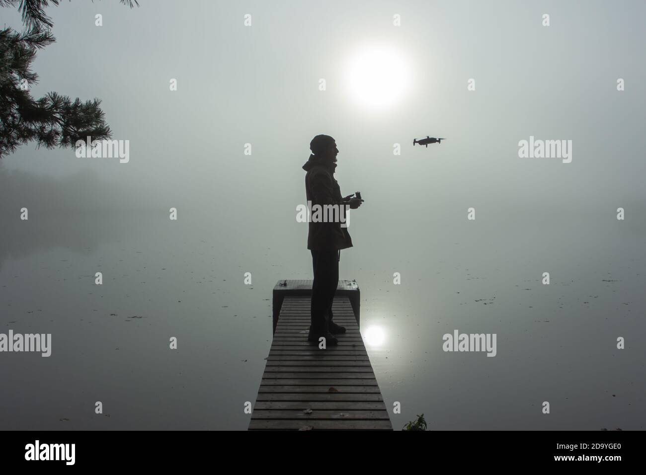 Man playing with the drone. Silhouette against the foggy landscape.Male operating the drone by remote control and having fun. Pilot flying drone. Use Stock Photo