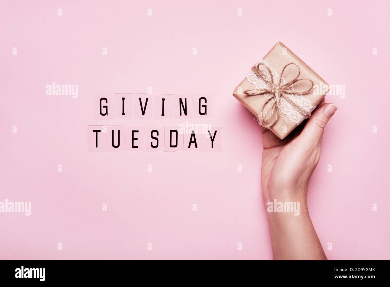 Giving Tuesday. Global day of charitable giving after Black Friday shopping day. Woman hand holding gift box on pink background Stock Photo
