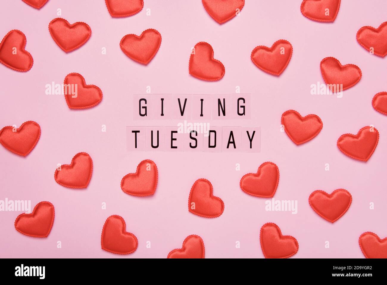 Giving Tuesday text message. Global day of charitable giving after Black Friday shopping day. Red hearts on pink background Stock Photo