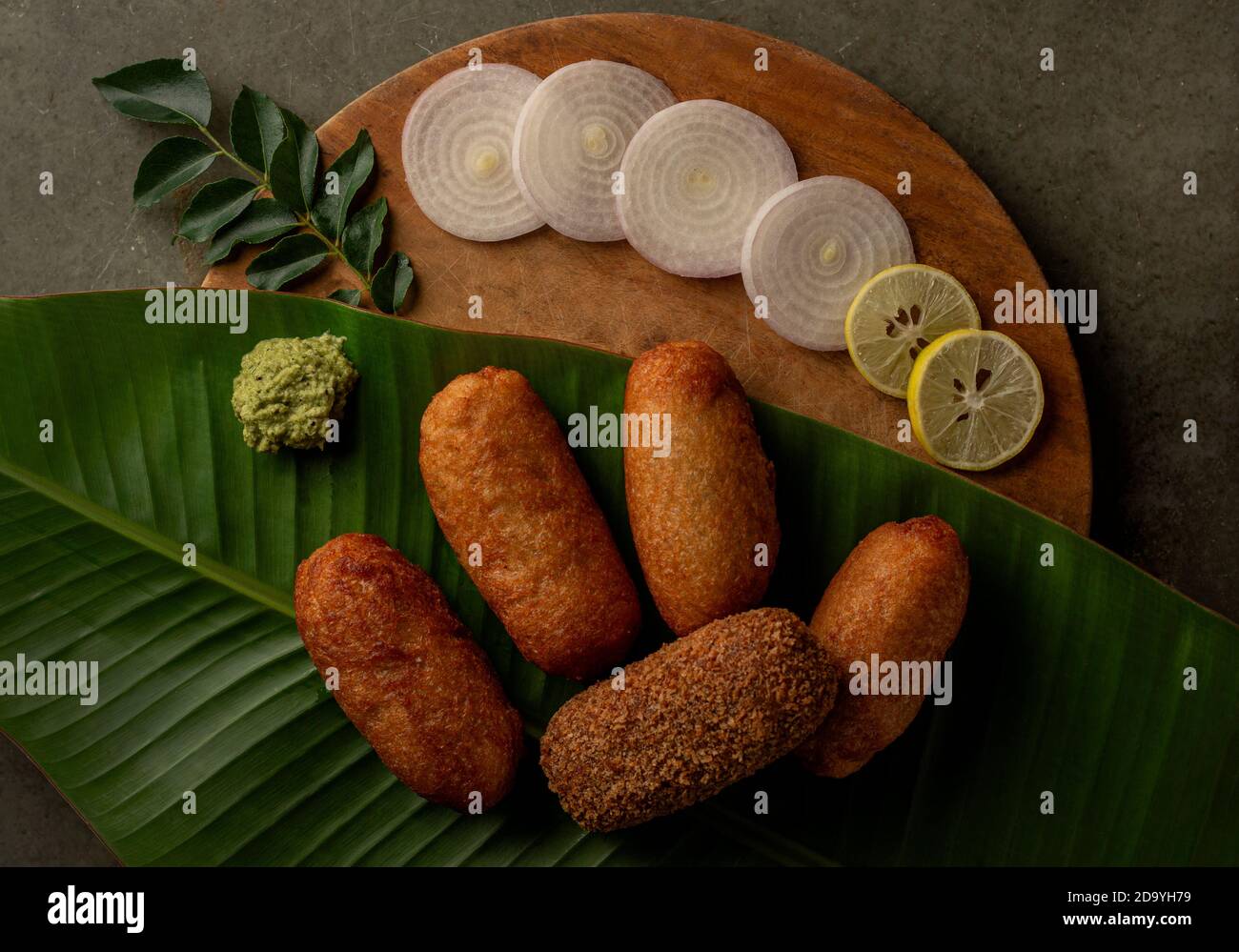 Potato bread roll on banana leaf and wooden base with onion, lemon and green chutney. Stock Photo