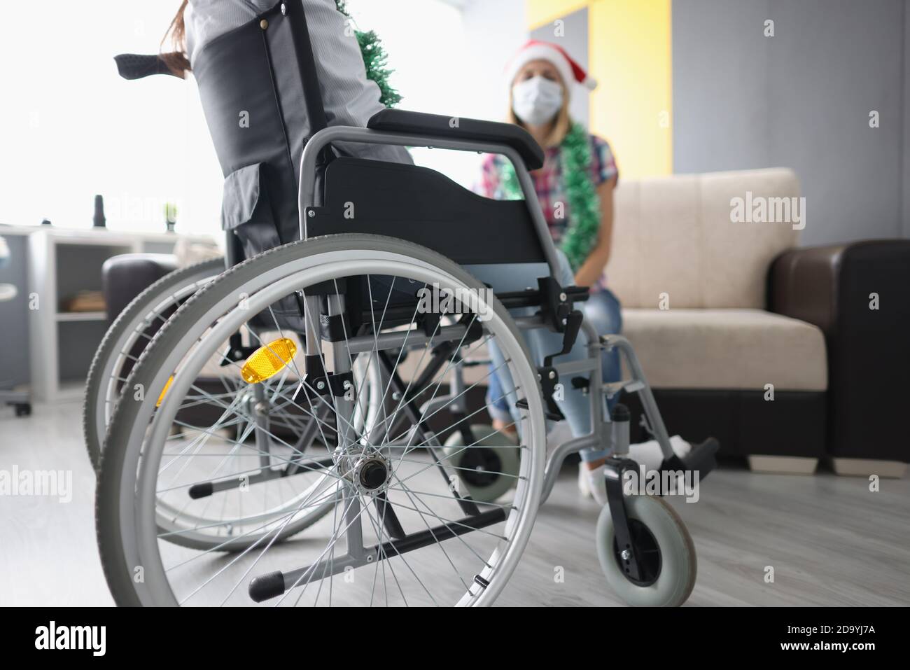 Man sits in a wheelchair in front of woman in santa claus hat and New Year's garland. Stock Photo