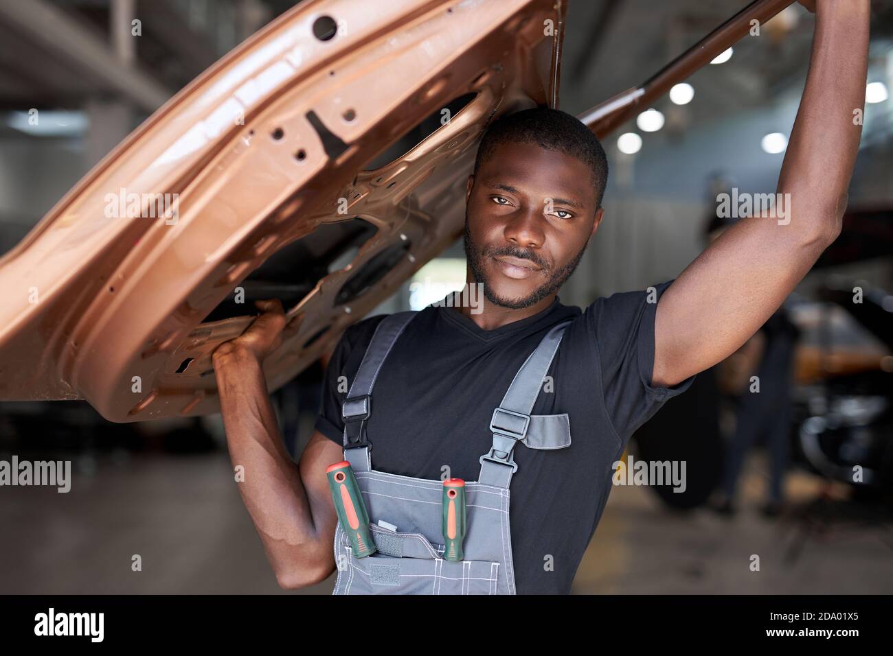confident auto mechanic holding seperate part of the car, going to