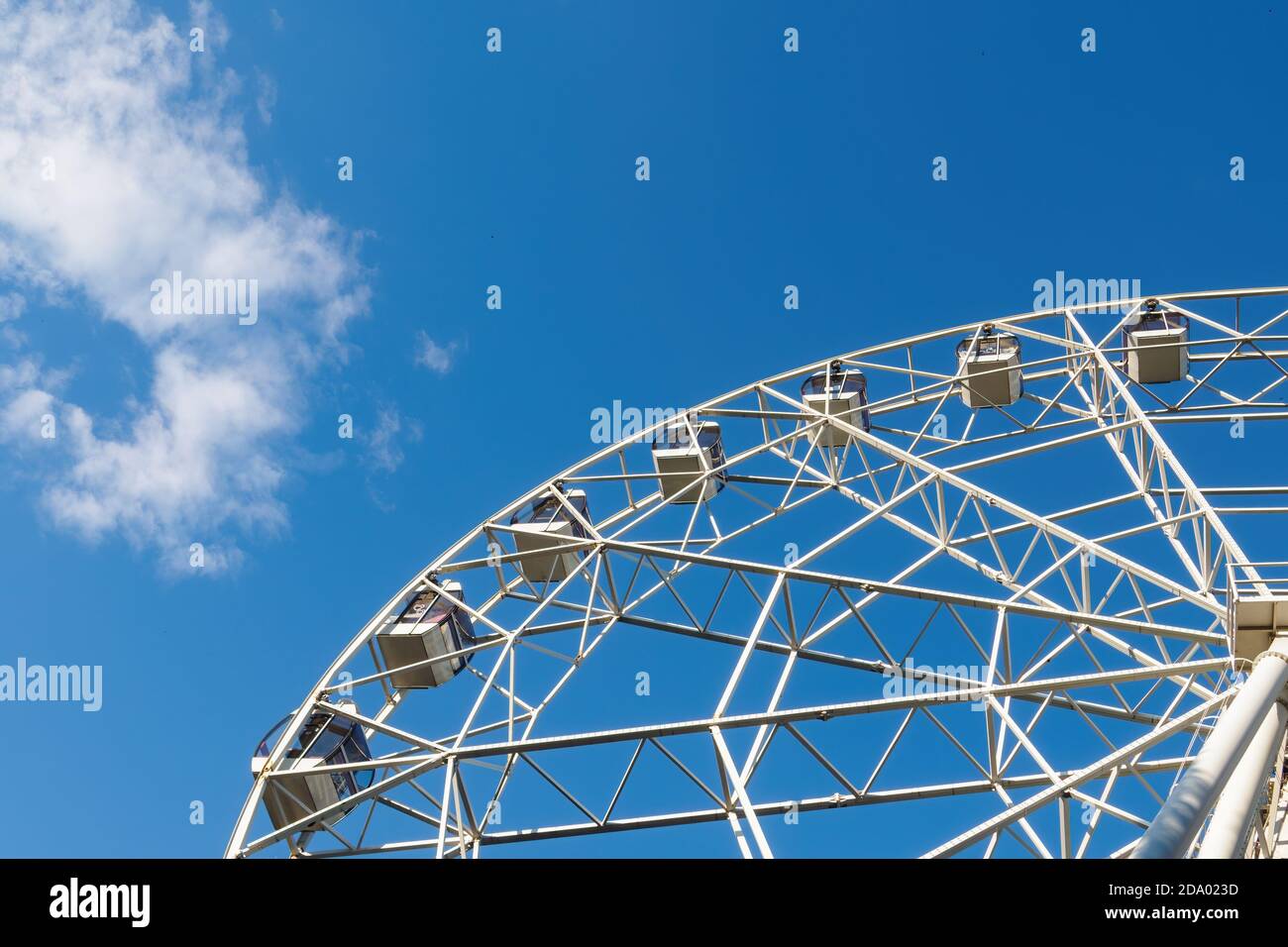 A part of white ferris wheel, cabins on background of blue sky and cloud in sunny summer day, bottom view. Stock Photo