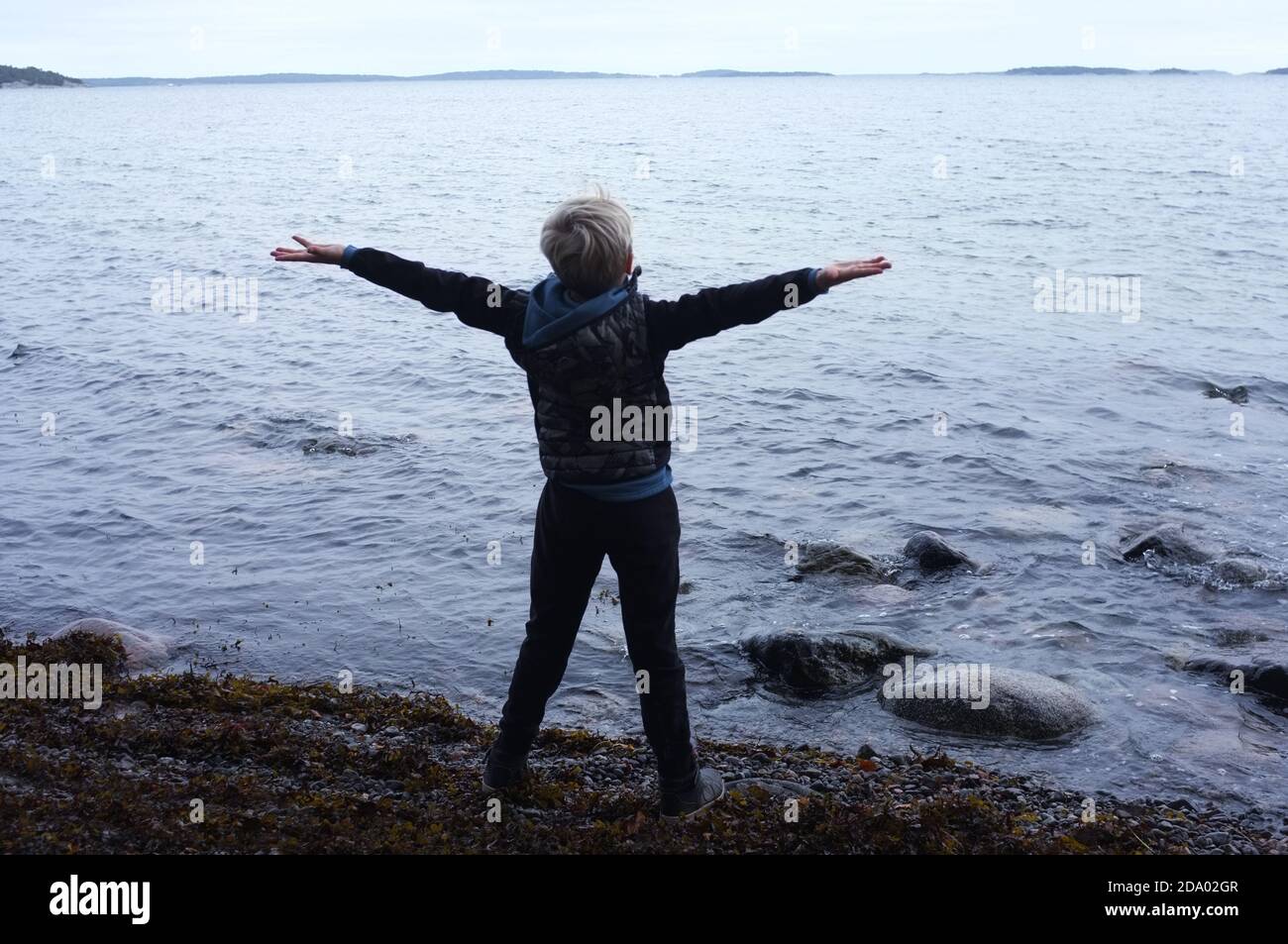 Blonde 7 year old boy in front of the water. Cherish the day! Open arms for the future. Stock Photo
